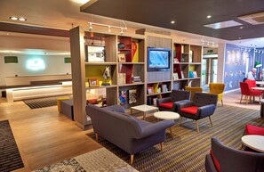 A modern lounge area with seating, a television, and a variety of books and decorative items. - Holiday Inn Northampton West M1, Jct 16 by IHG (Northampton)