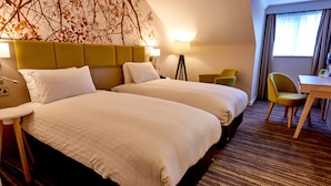 Une chambre d’hôtel avec deux lits, un bureau, une chaise et une lampe.
