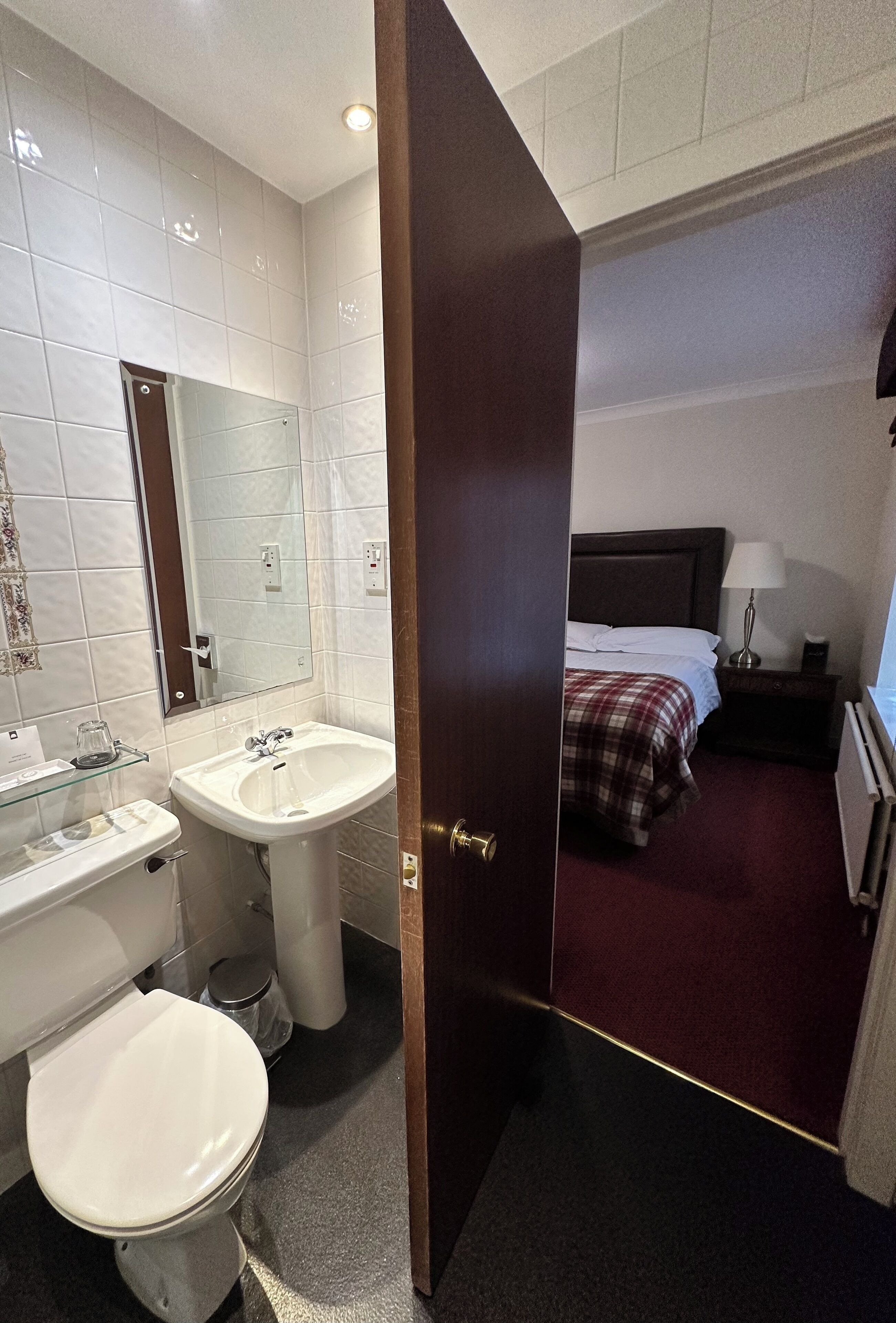 A hotel bathroom with a toilet, sink, and mirror.
