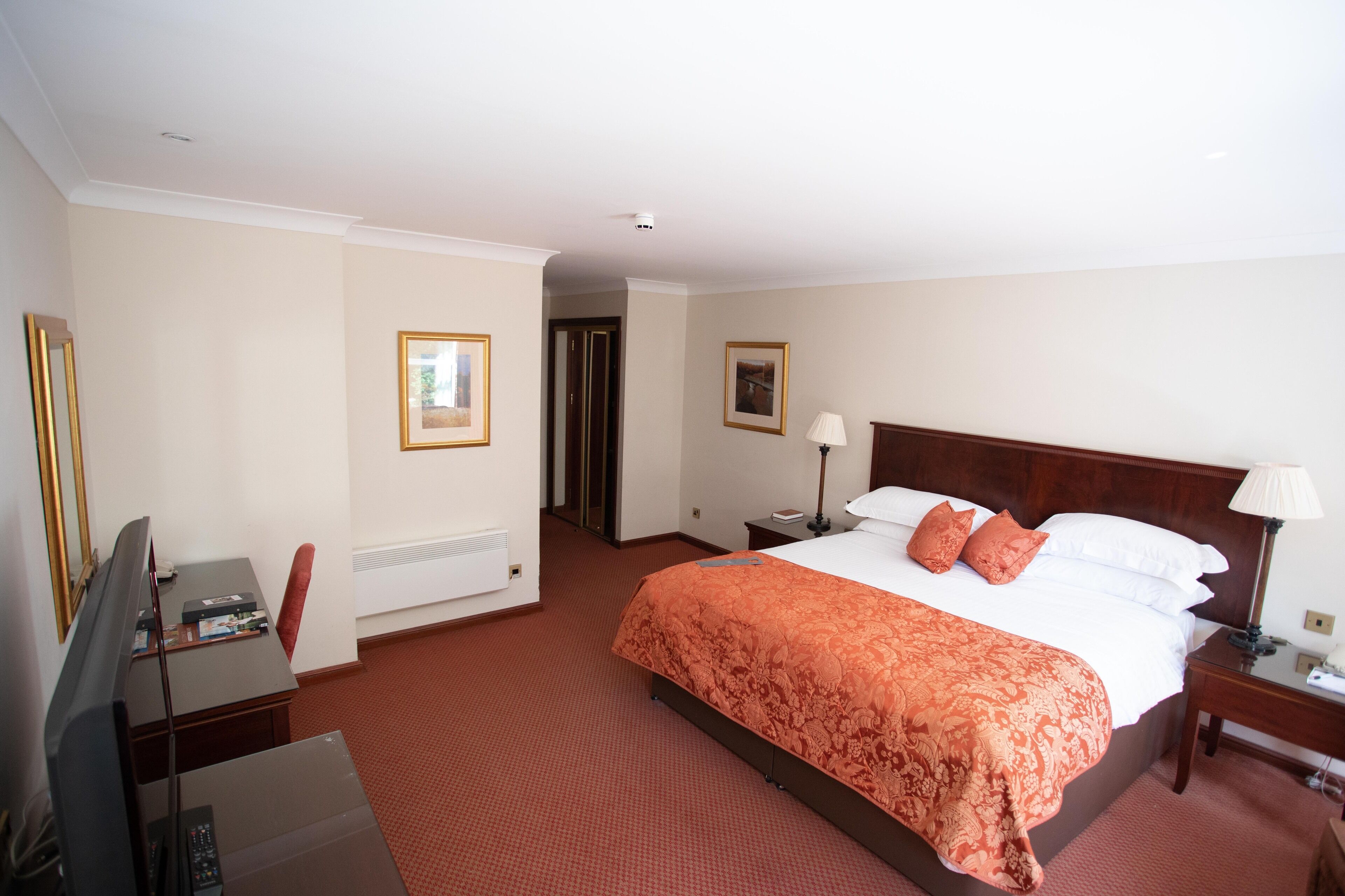 A hotel room with a large bed, a desk with a computer, a television, and a door leading to another room.
