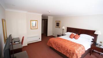 A hotel room with a large bed, a desk with a computer, a television, and a door leading to another room.