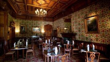 A dining area with wooden furniture, floral wallpaper, and a chandelier.