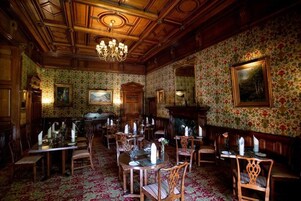 A dining area with wooden furniture, floral wallpaper, and a chandelier.