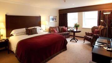 A hotel room with a large bed, a sofa, a small table, and a desk with a lamp.