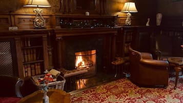 A cozy room with a fireplace, leather armchairs, a patterned rug, and two lamps.