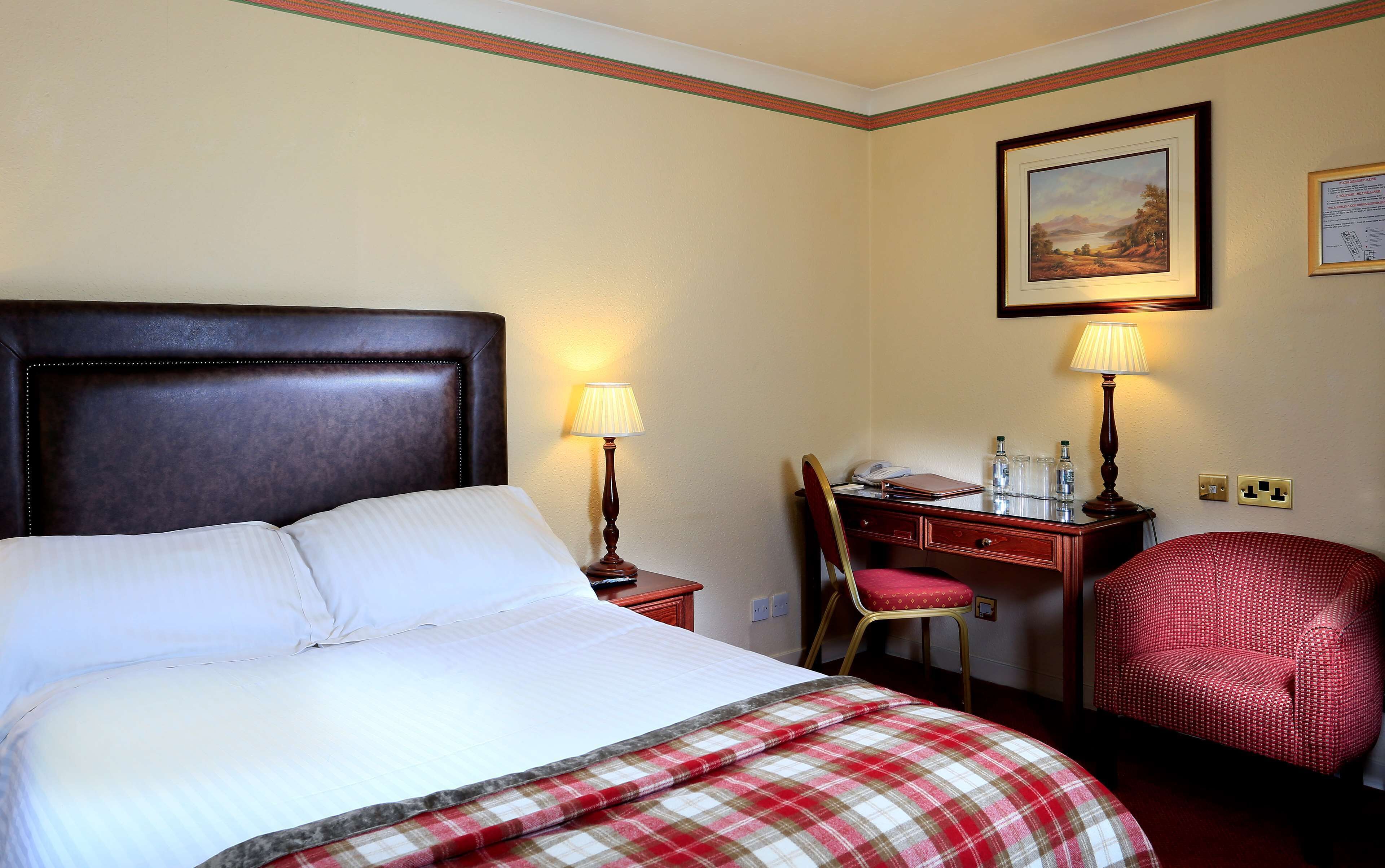 A hotel room with a large bed, two bedside lamps, a desk with a chair, and a framed picture on the wall.