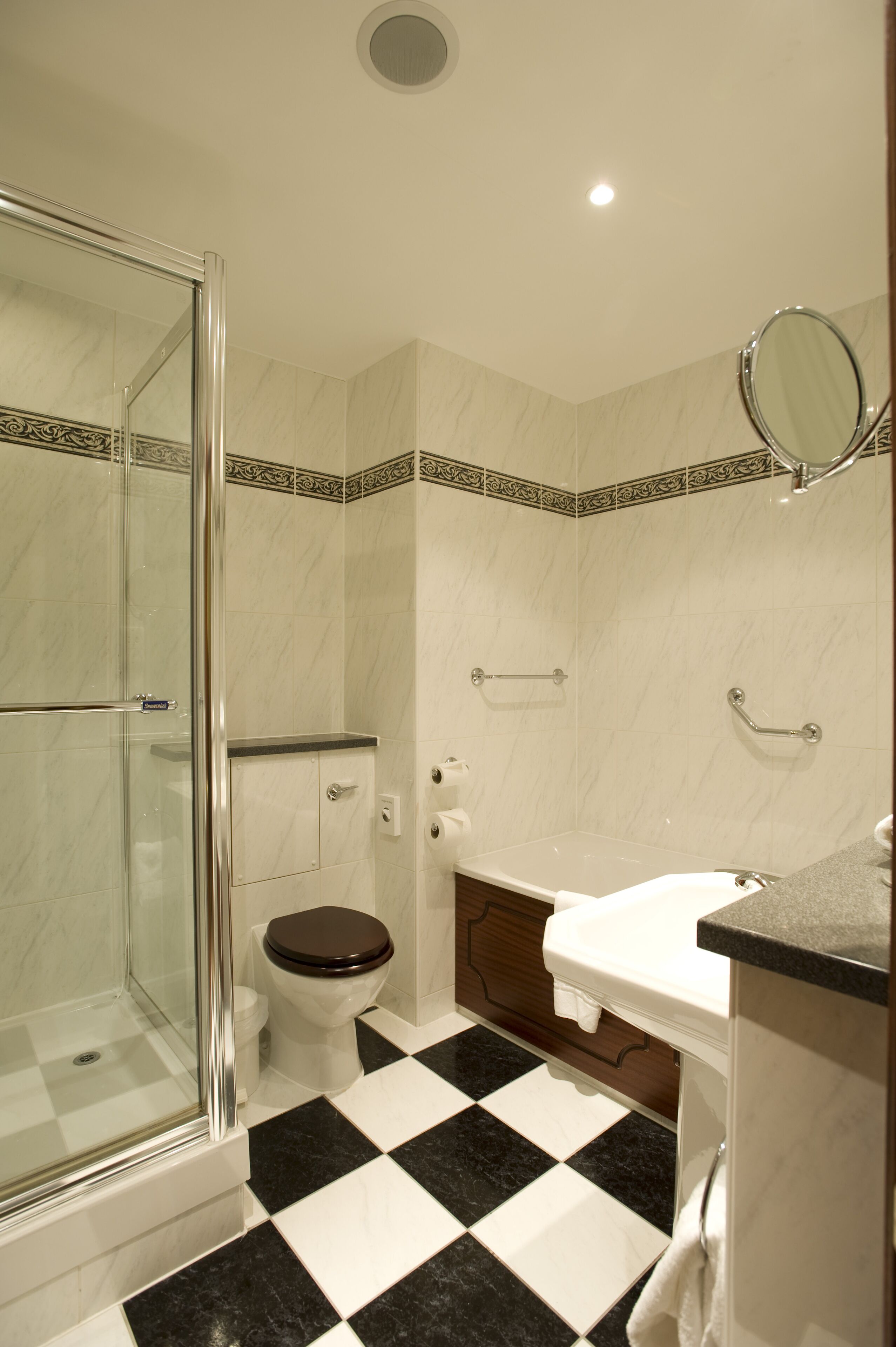 A bathroom with a glass-enclosed shower, a toilet with a brown seat, a white sink, and a mirror on the wall.