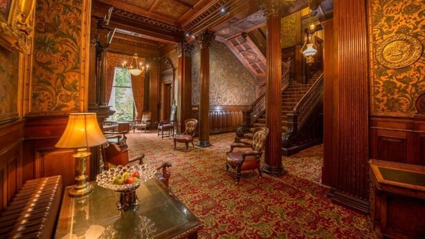 Una sala imponente con paneles de madera decorados, un piano y una escalera que conduce a un nivel superior.