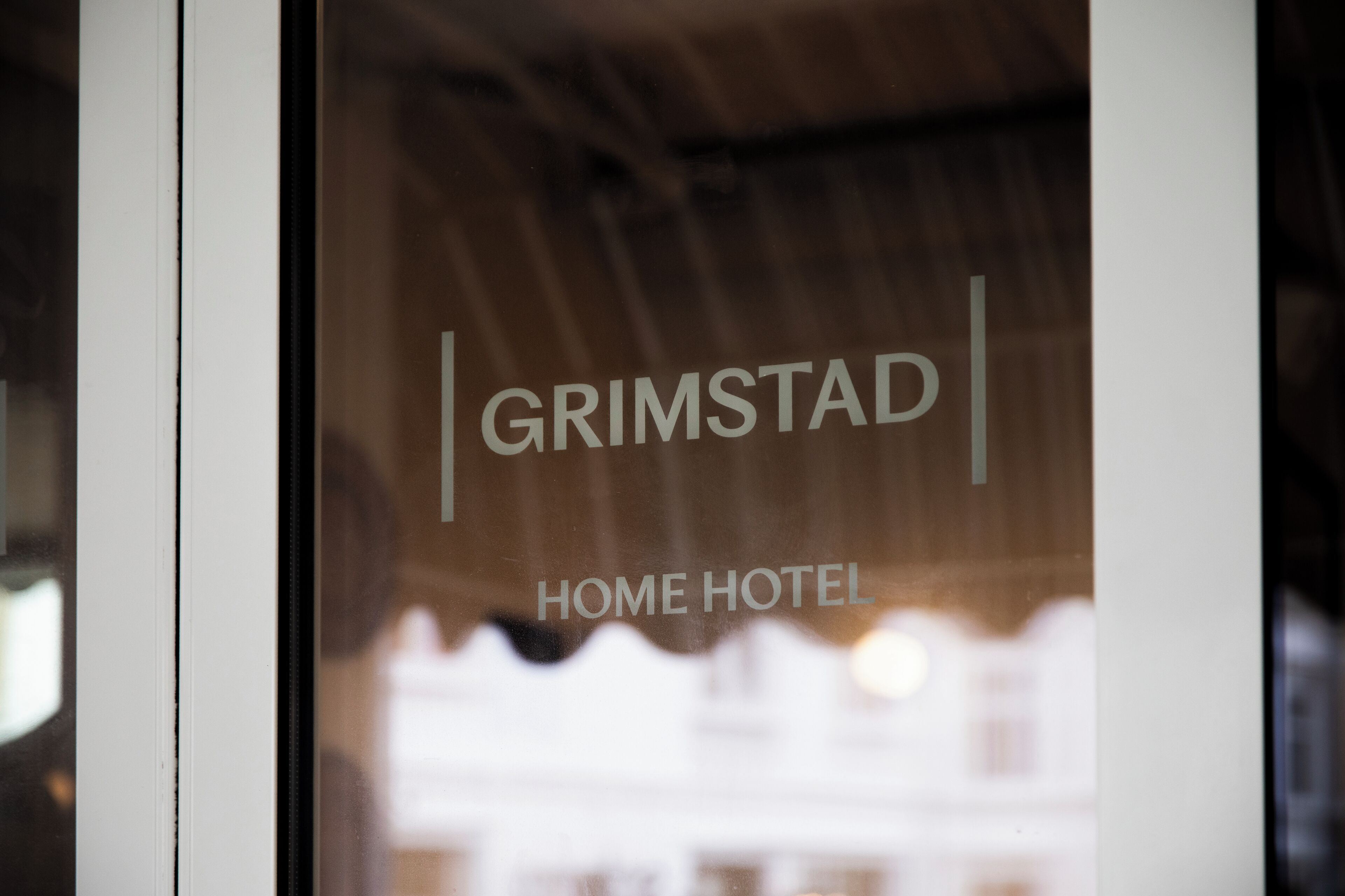 A window with the text "GRIMSTAD HOME HOTEL" visible through the glass.