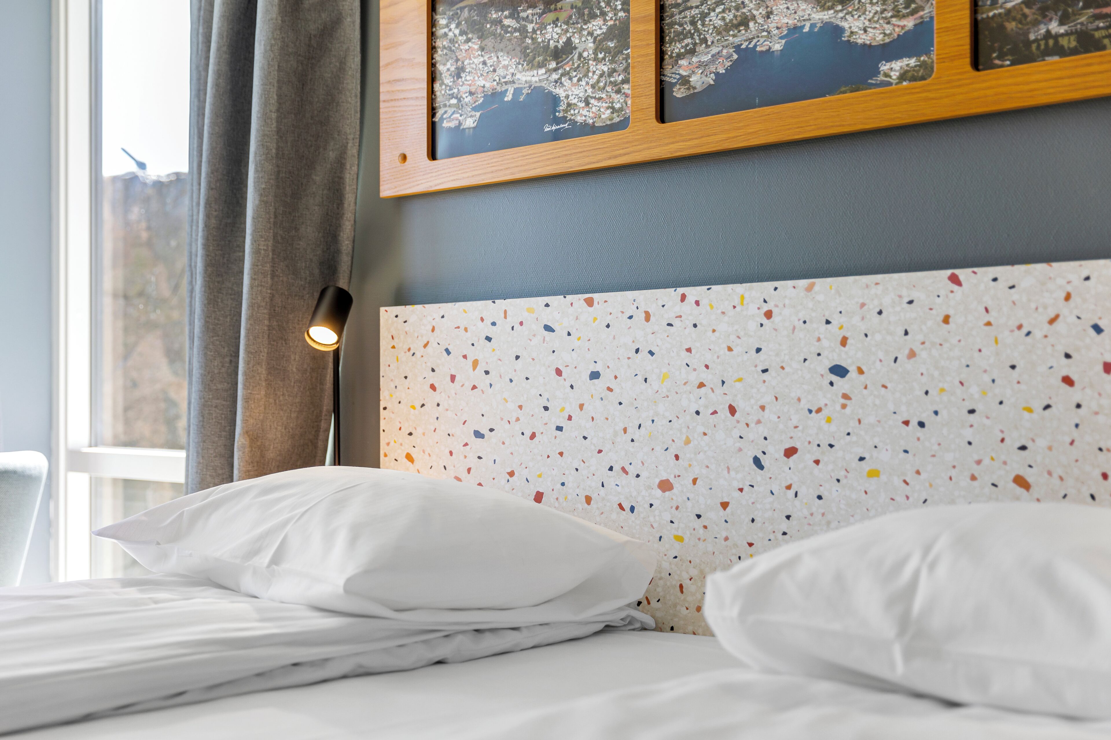 Un lit bien fait, avec du linge de lit blanc, une tête de lit à motifs et une fenêtre avec des rideaux.