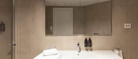 A modern bathroom with a white sink, mirror, and two bottles of shampoo.