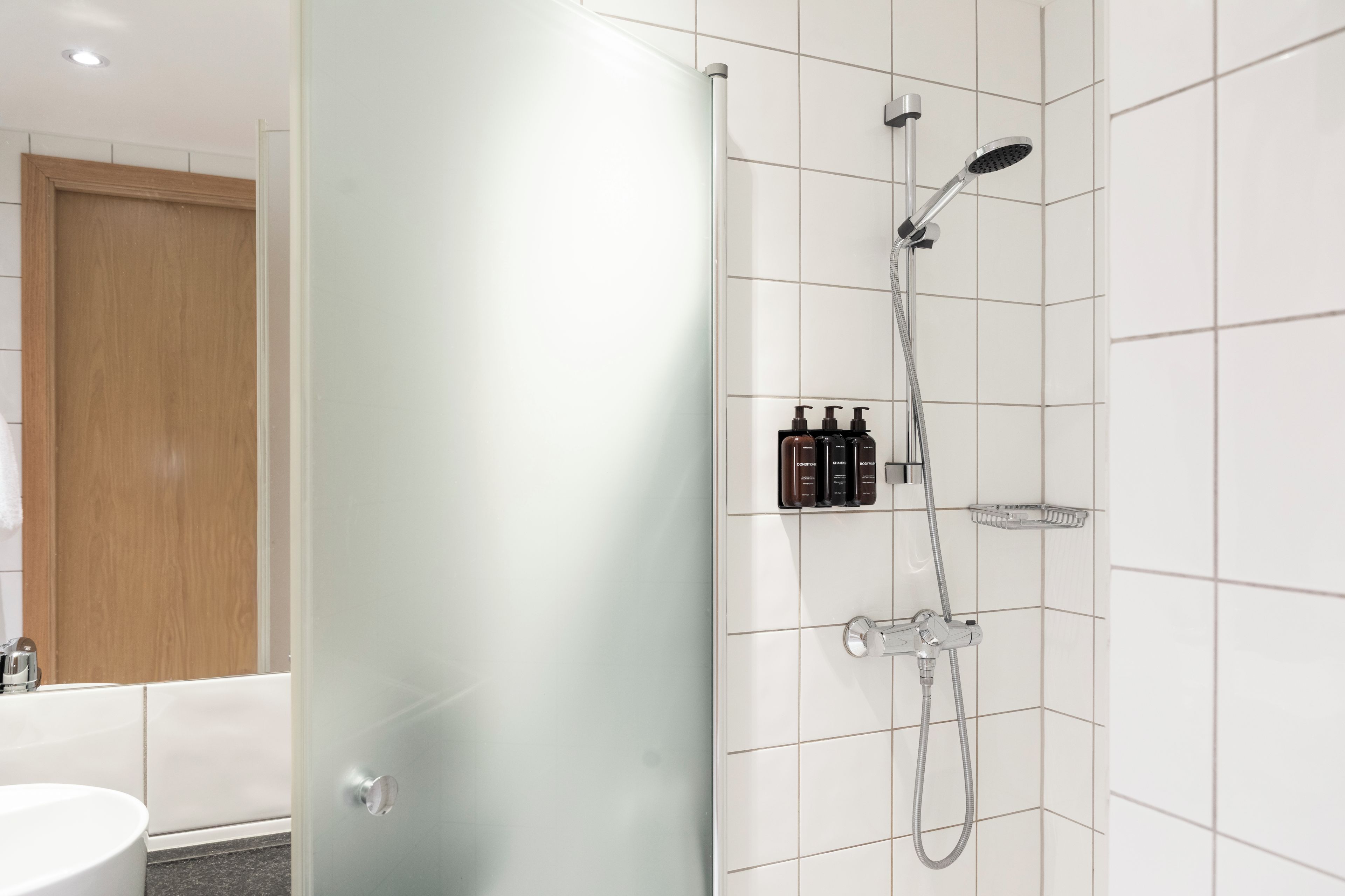 Une salle de bain moderne avec une douche à parois de verre, un lavabo blanc et une porte en bois.
