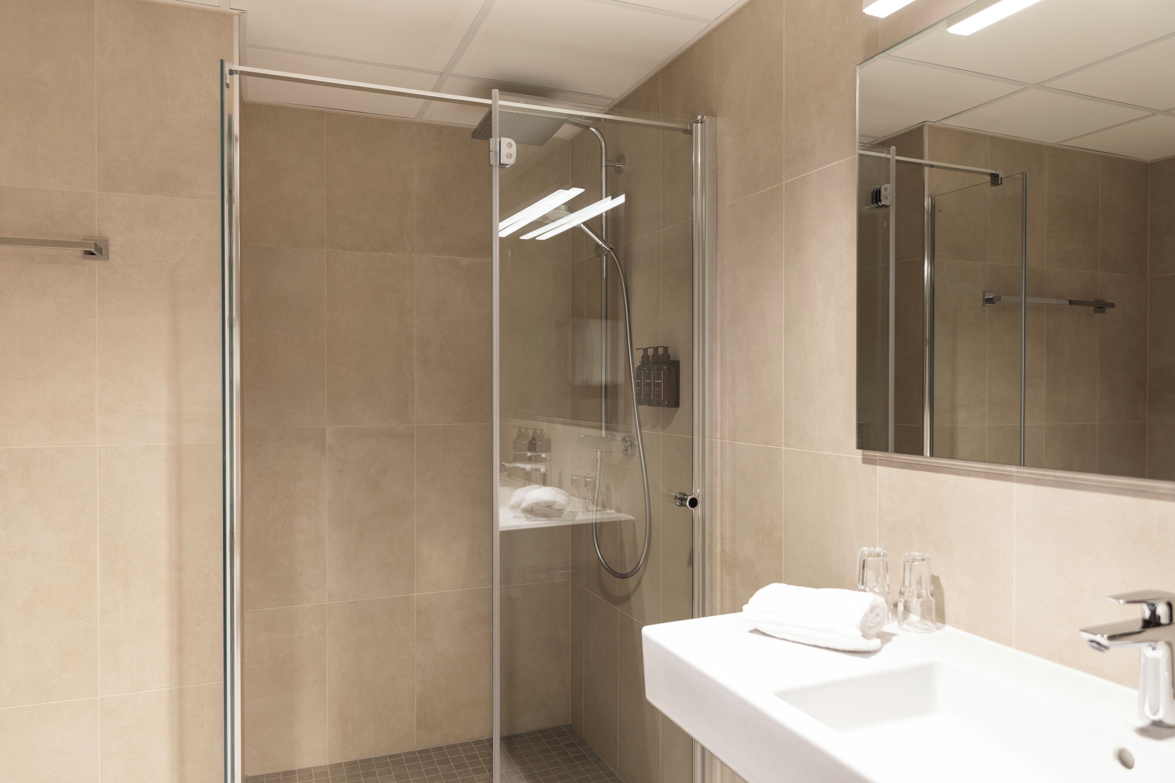 Ein modernes Badezimmer mit einer Glaskabine zur Dusche, einem weißen Waschbecken und einem großen Spiegel.