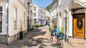 A narrow cobblestone street lined with historic buildings, a cyclist with a backpack, and a wooden door with a coat of arms. - Home Hotel Grimstad (Grimstad)