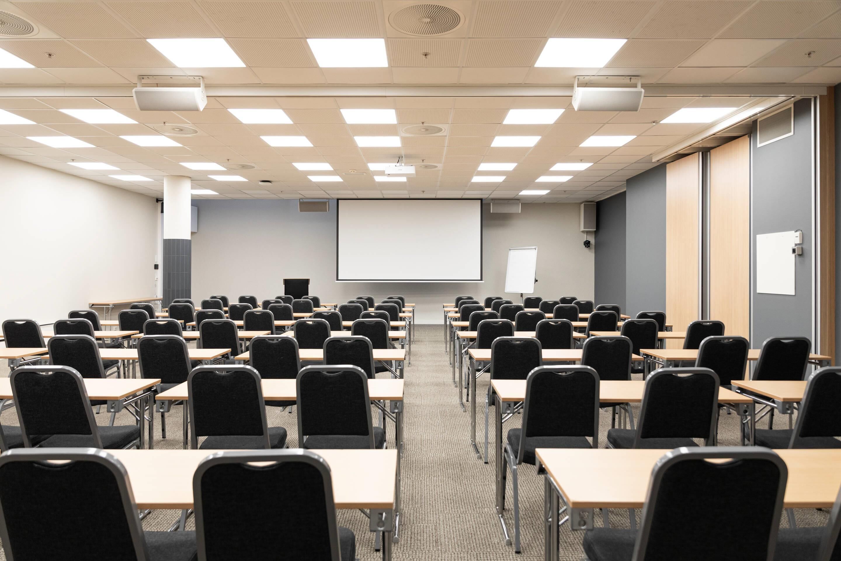 A conference room with rows of tables and chairs, a projector screen, and a whiteboard.