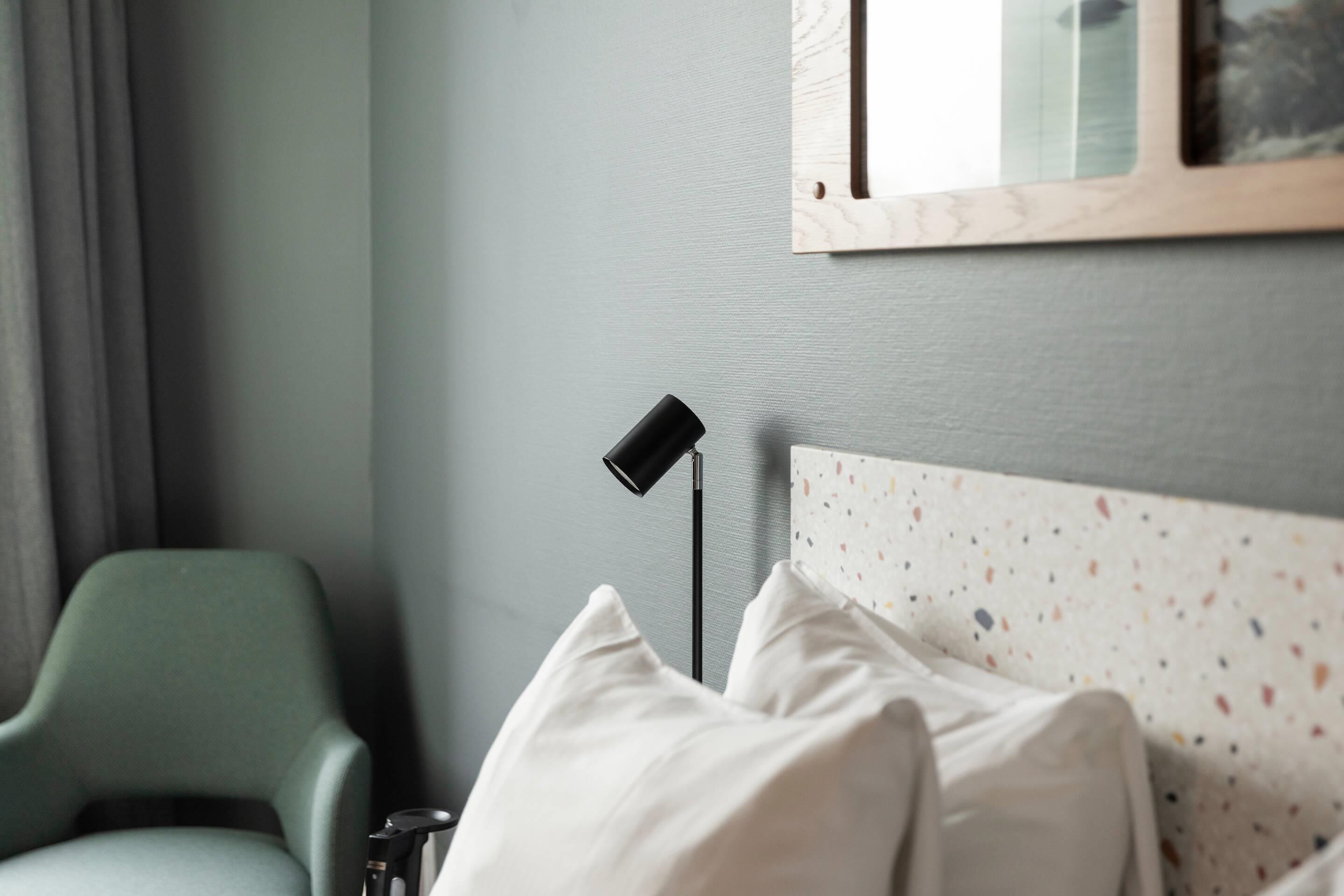 Ein Schlafzimmer mit einem grünen Sessel, einer Nachttischlampe und einem Bett mit gemustertem Kopfteil.