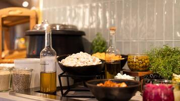 Una encimera de cocina con diversos alimentos y recipientes, incluyendo una botella de aceite de oliva, tazones de comida y frascos de aceitunas y encurtidos.