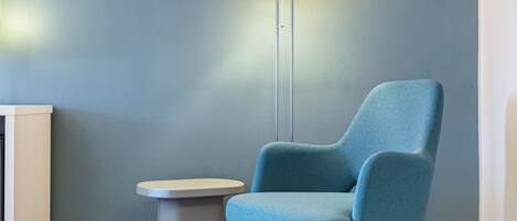 Una habitación con un sillón azul, una mesita blanca y una lámpara de pie frente a una pared azul.