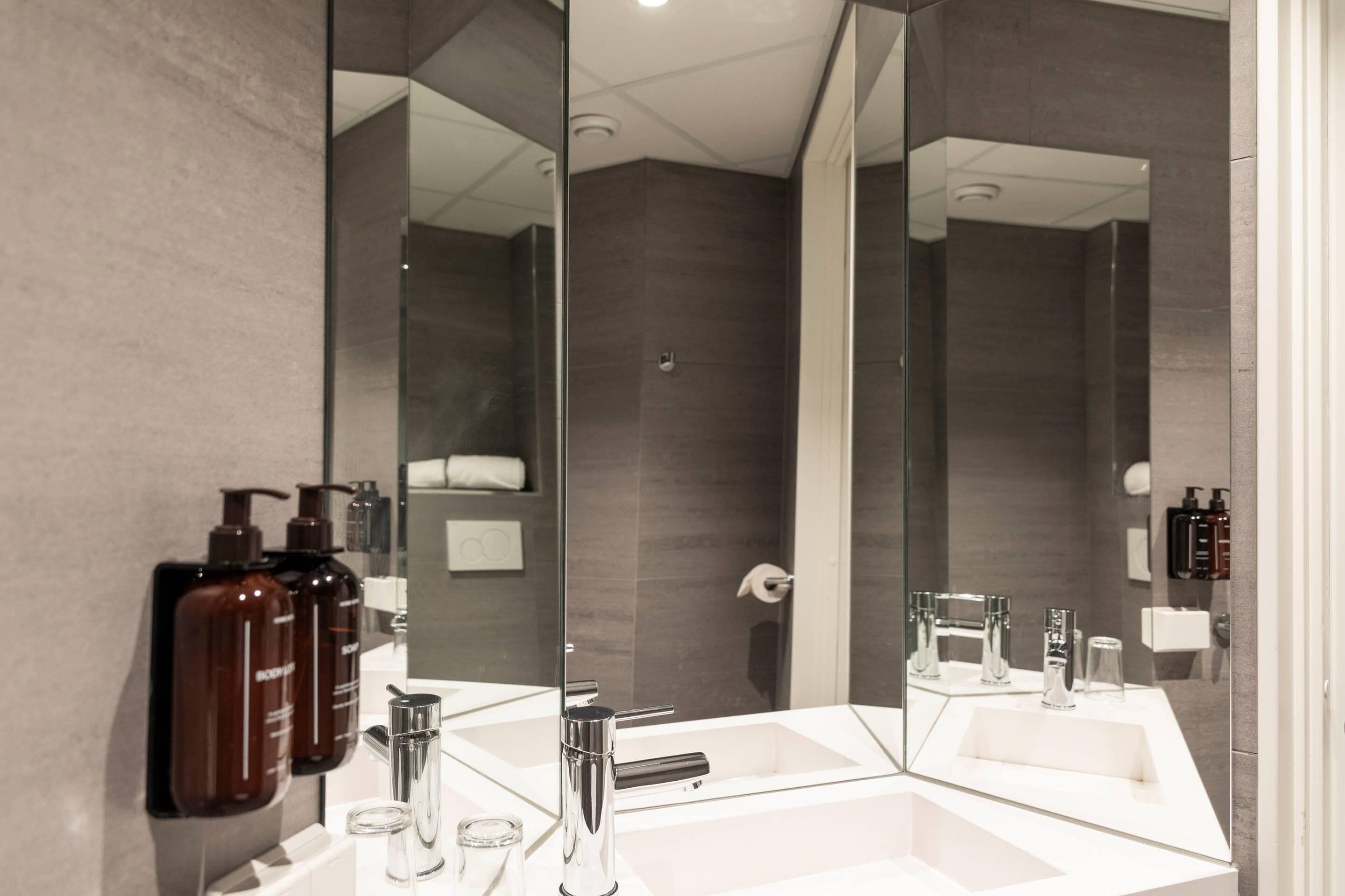 A modern bathroom with a large mirror, a white sink, and a shower area.