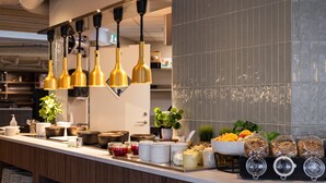 A modern kitchen with a long counter, gold pendant lights, and various food items displayed. - Home Hotel Grimstad (Grimstad)