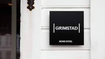 Un letrero negro con texto blanco que dice 'GRIMSTAD HOME HOTEL' montado sobre una pared blanca.