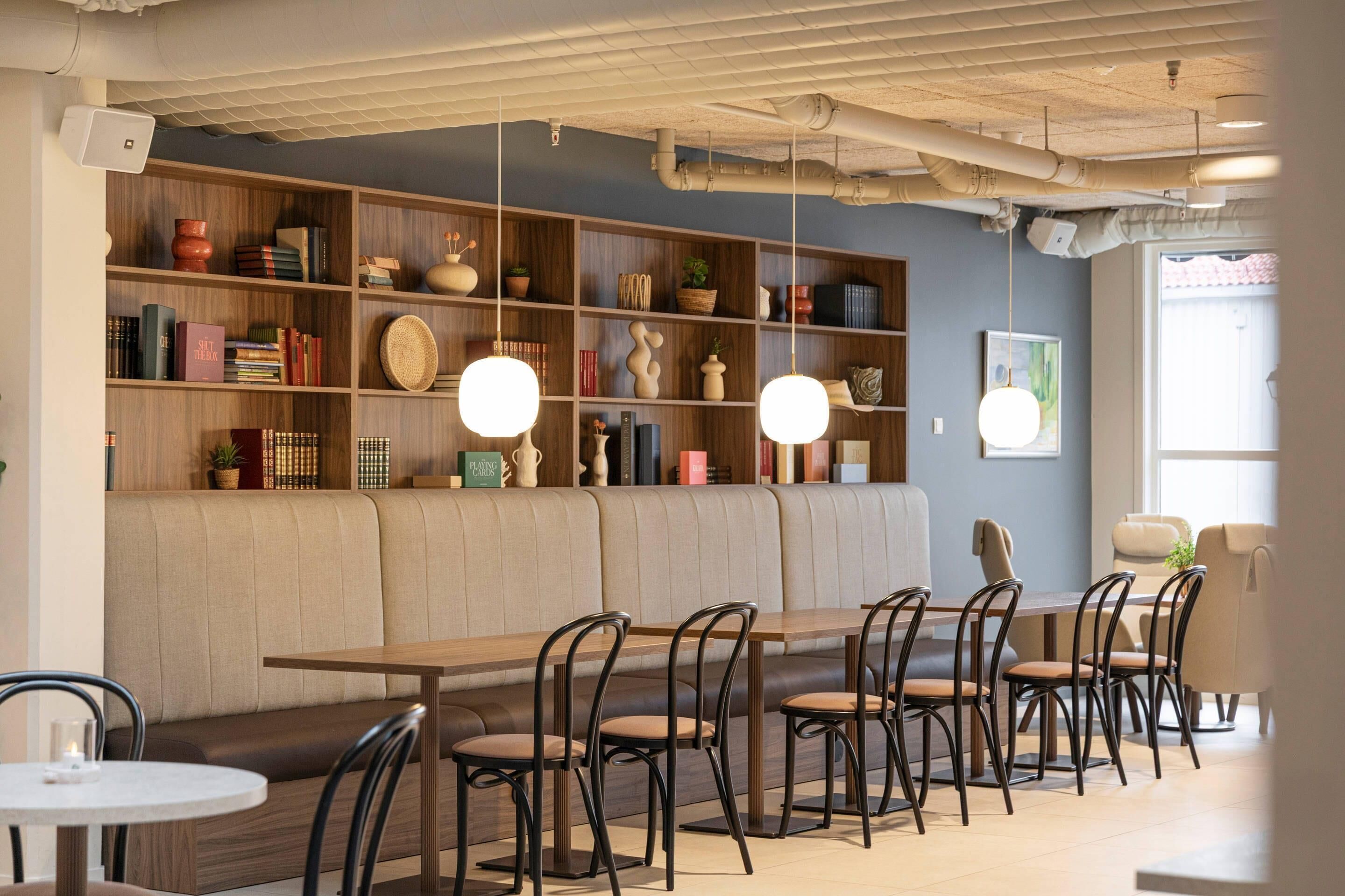 A modern interior with a wooden bookshelf, a bench, and a dining area with chairs and a table.