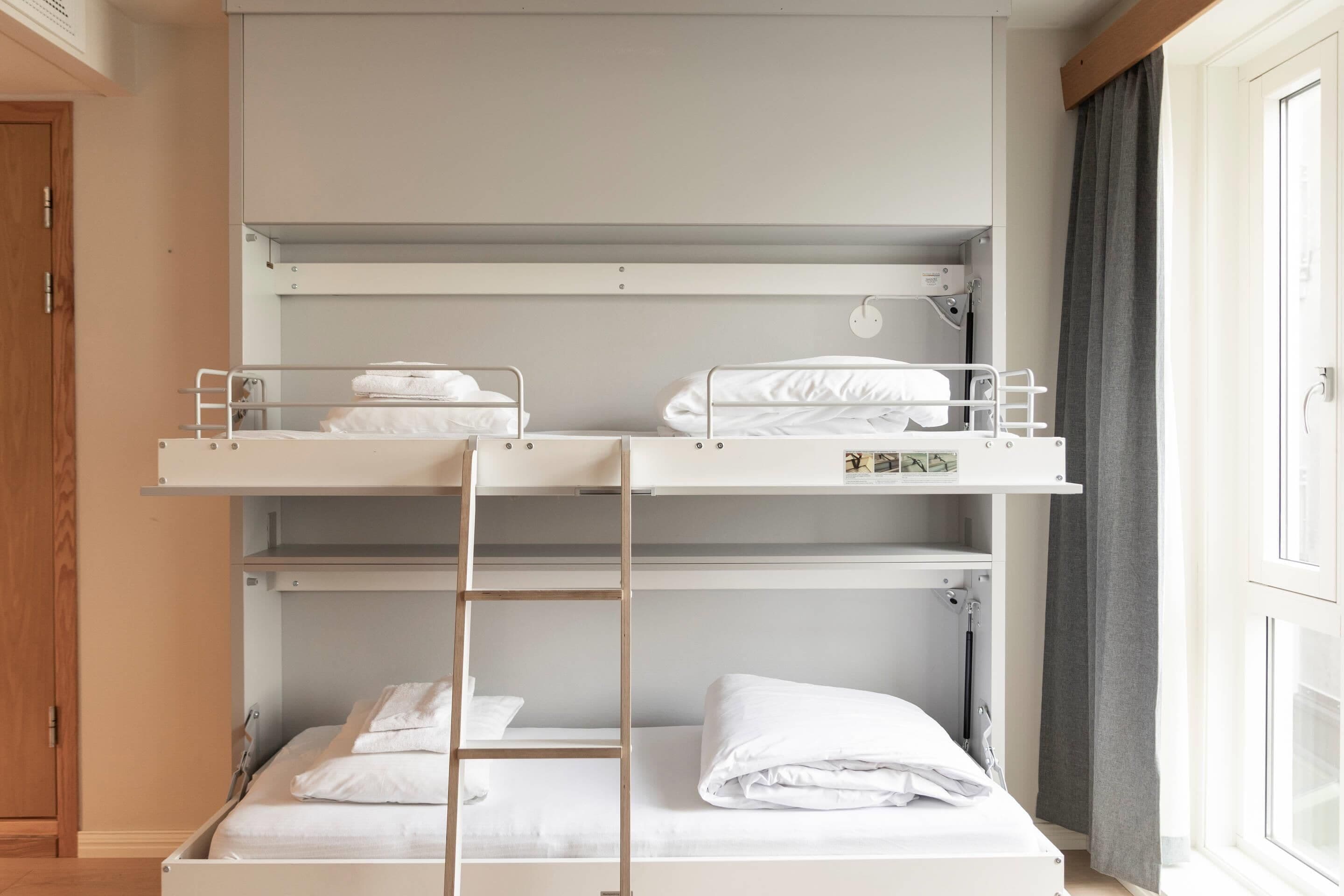 A bunk bed room with a ladder, a wooden door, and a window with curtains.