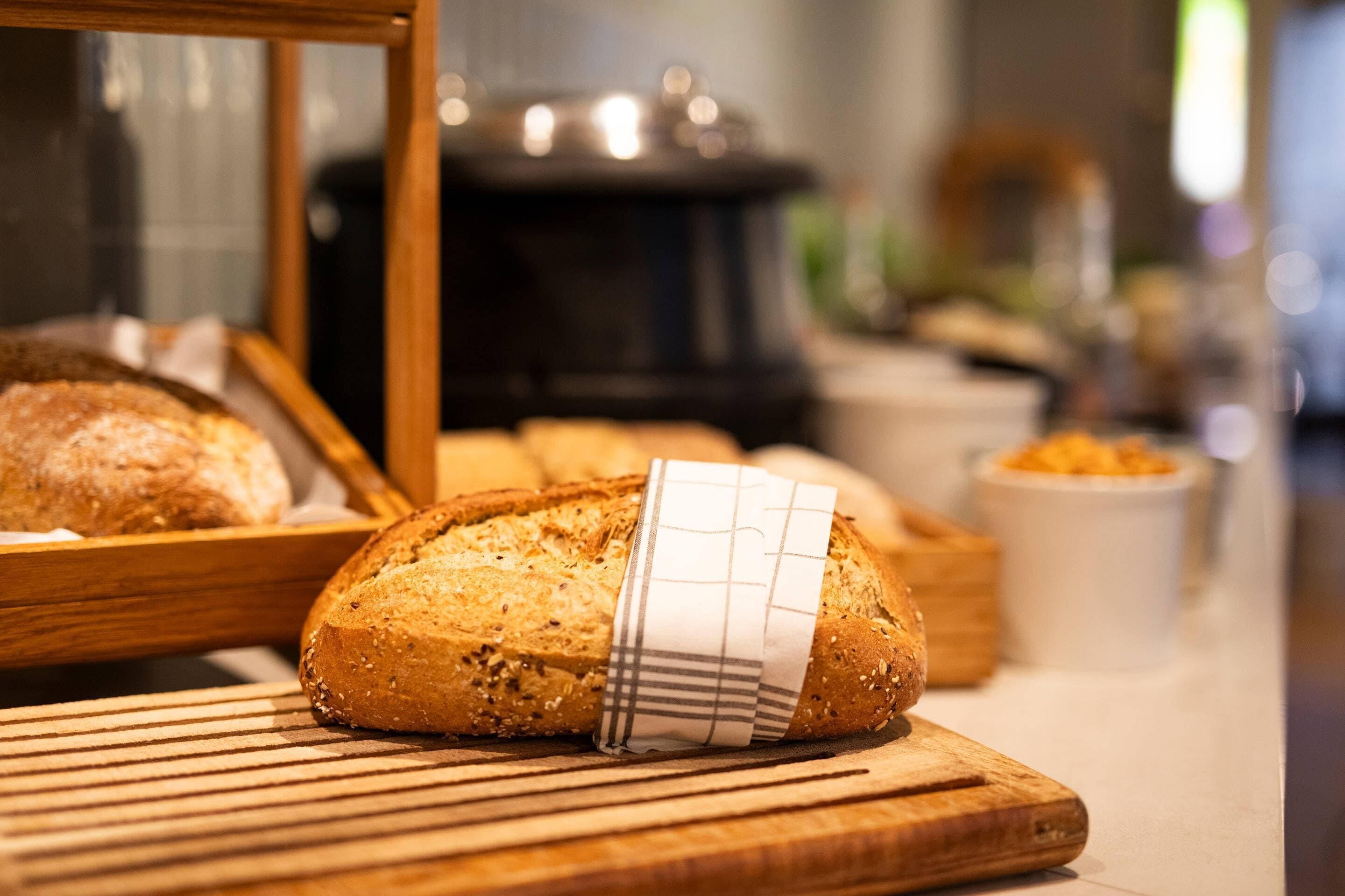 Une miche de pain sur une planche à découper en bois, entourée d’un tissu.