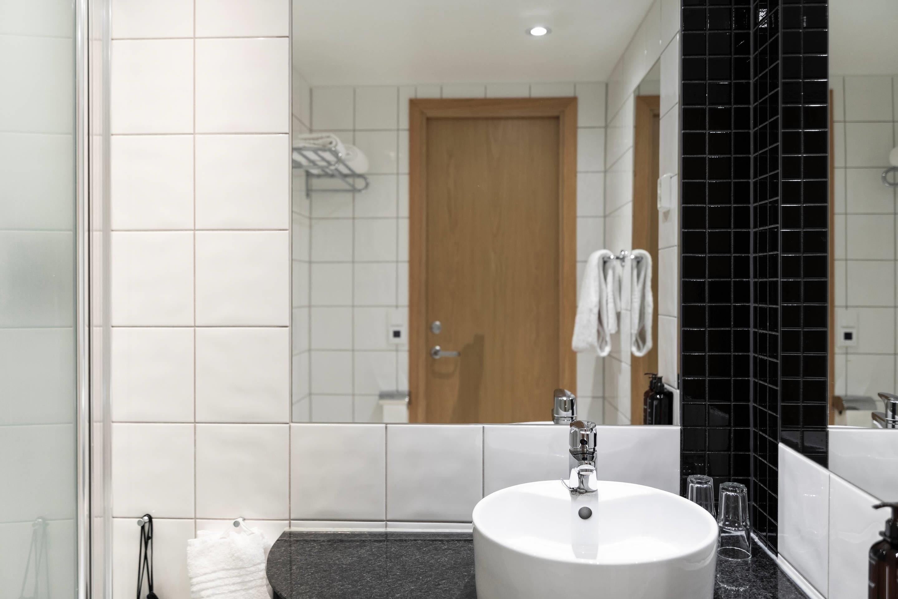 A modern bathroom with a white sink, black tiled backsplash, and a wooden door.