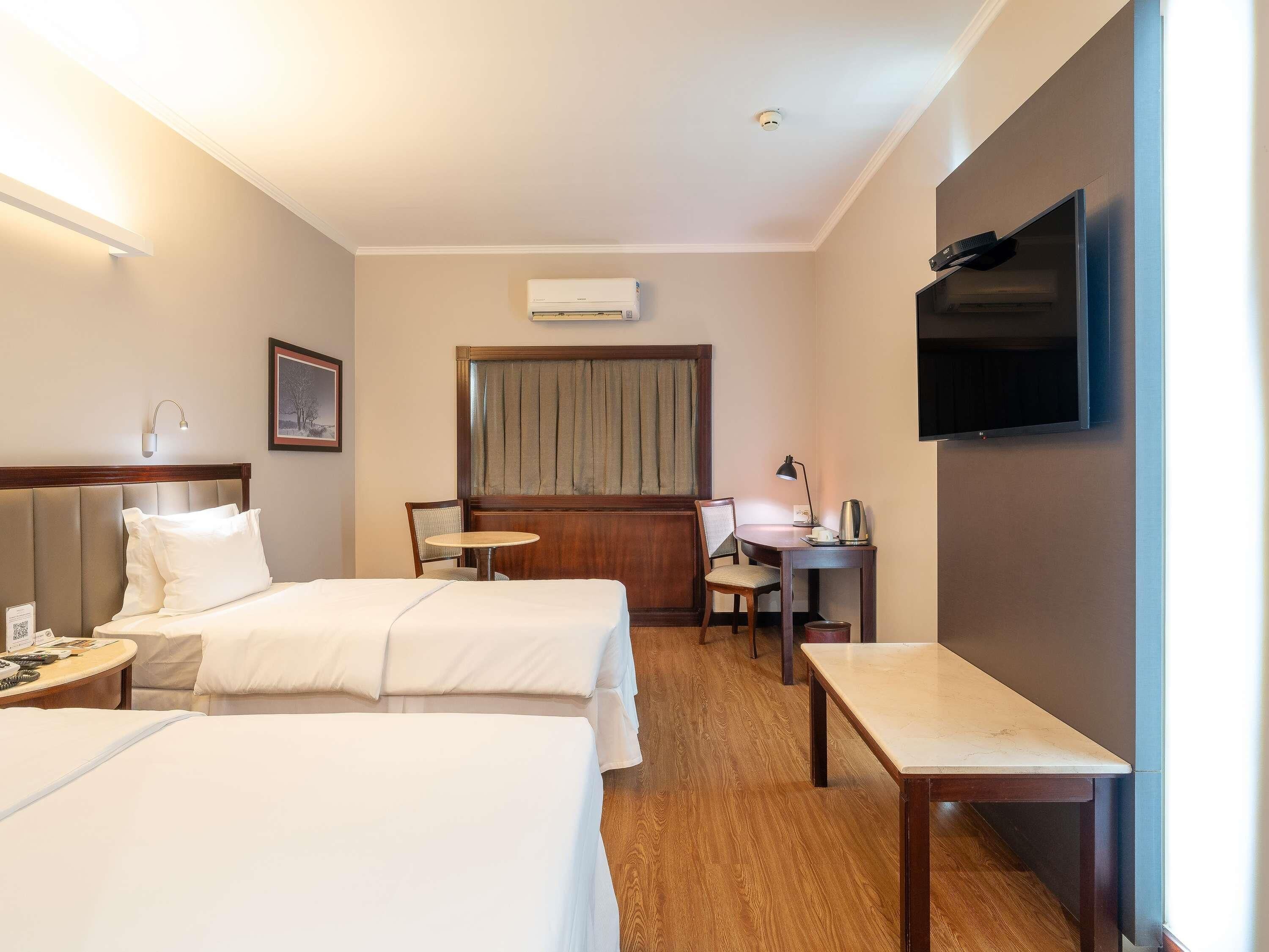 Habitación de hotel con dos camas, un escritorio, una silla, un televisor y un equipo de aire acondicionado.