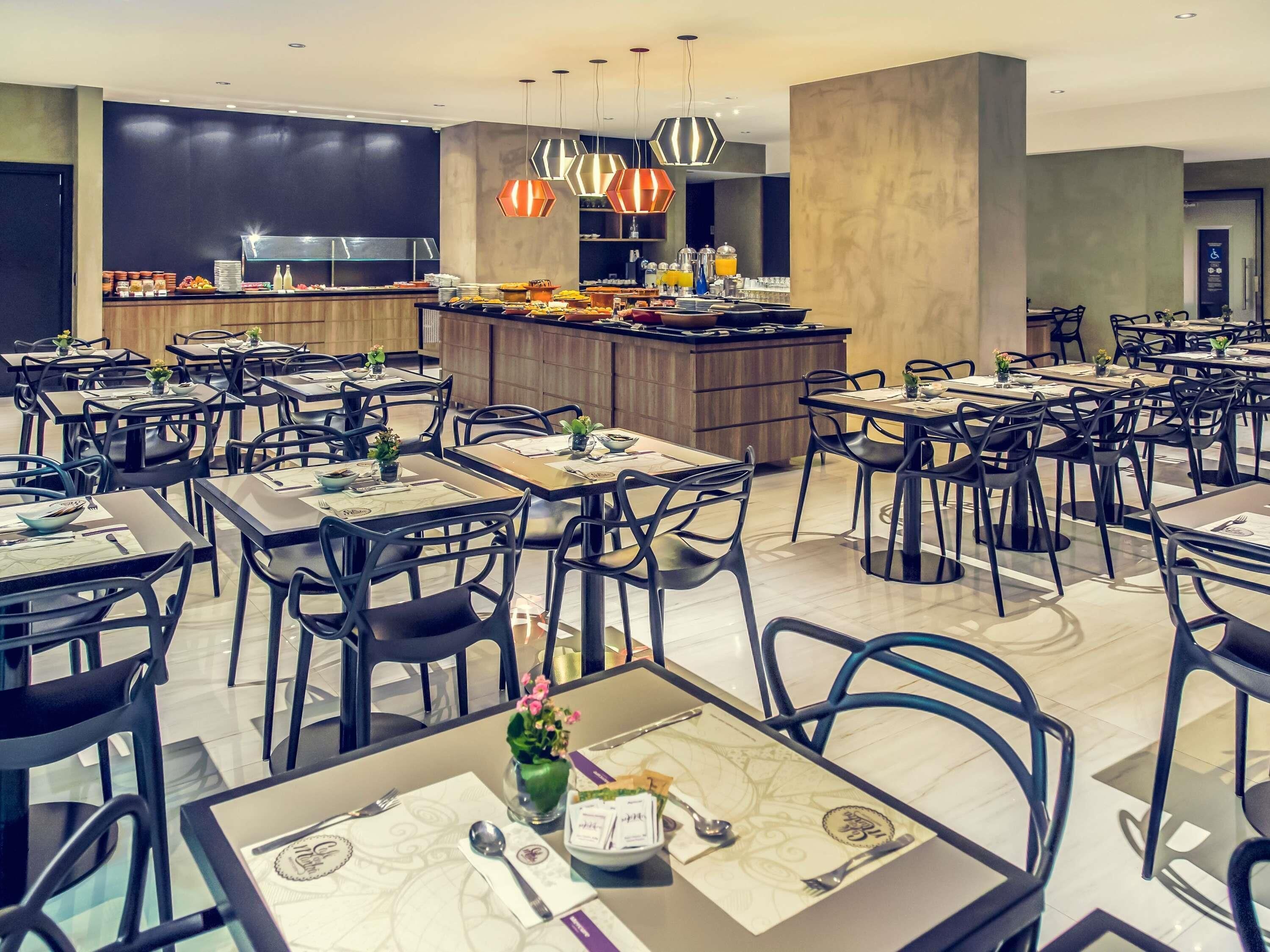 Un comedor moderno con varias mesas y sillas, una barra central e iluminación colgante.