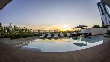 Piscina no terraço com cadeiras de sol e vista para o pôr do sol.