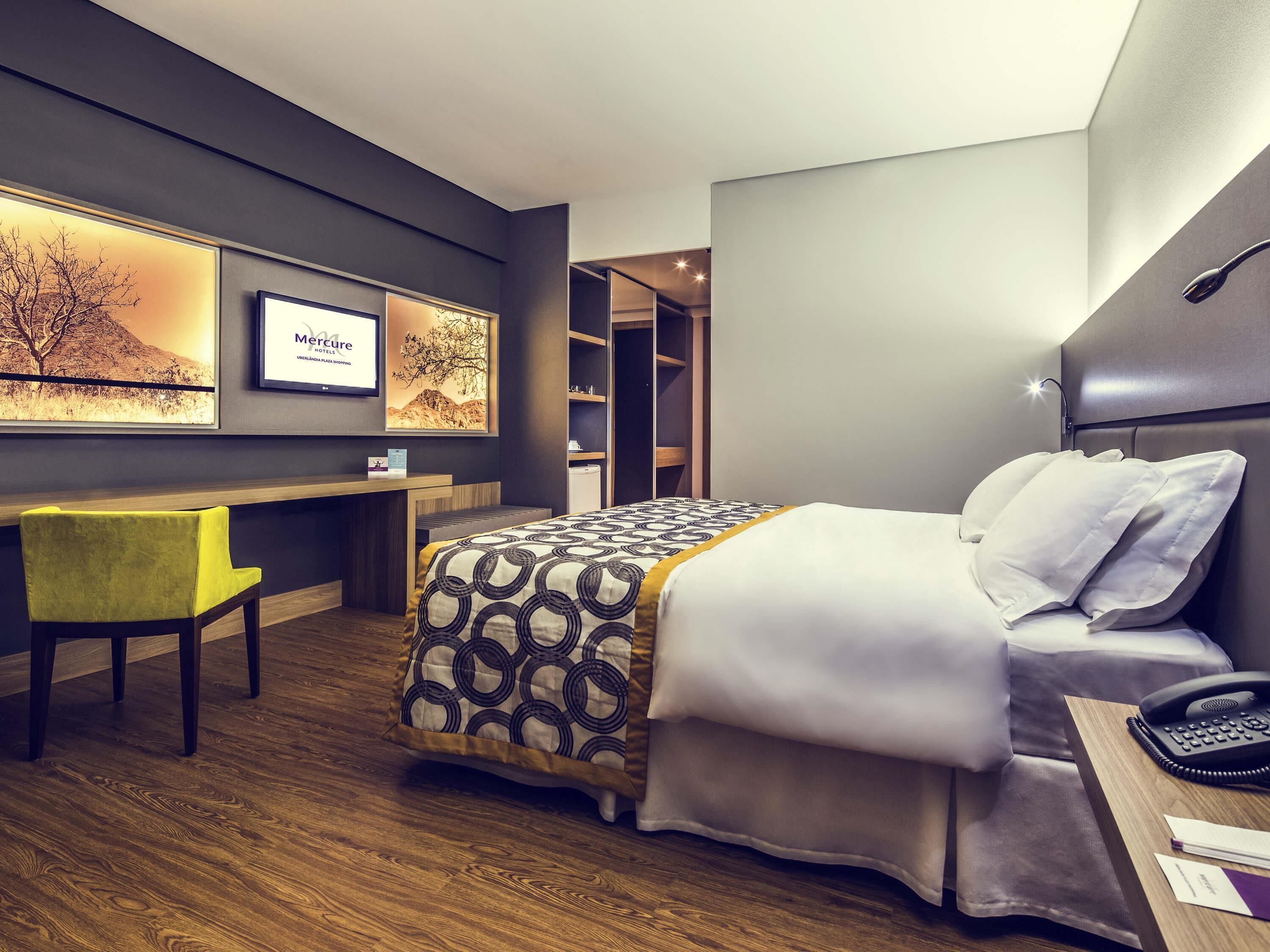 A hotel room with a bed, desk, chair, and a framed picture on the wall.