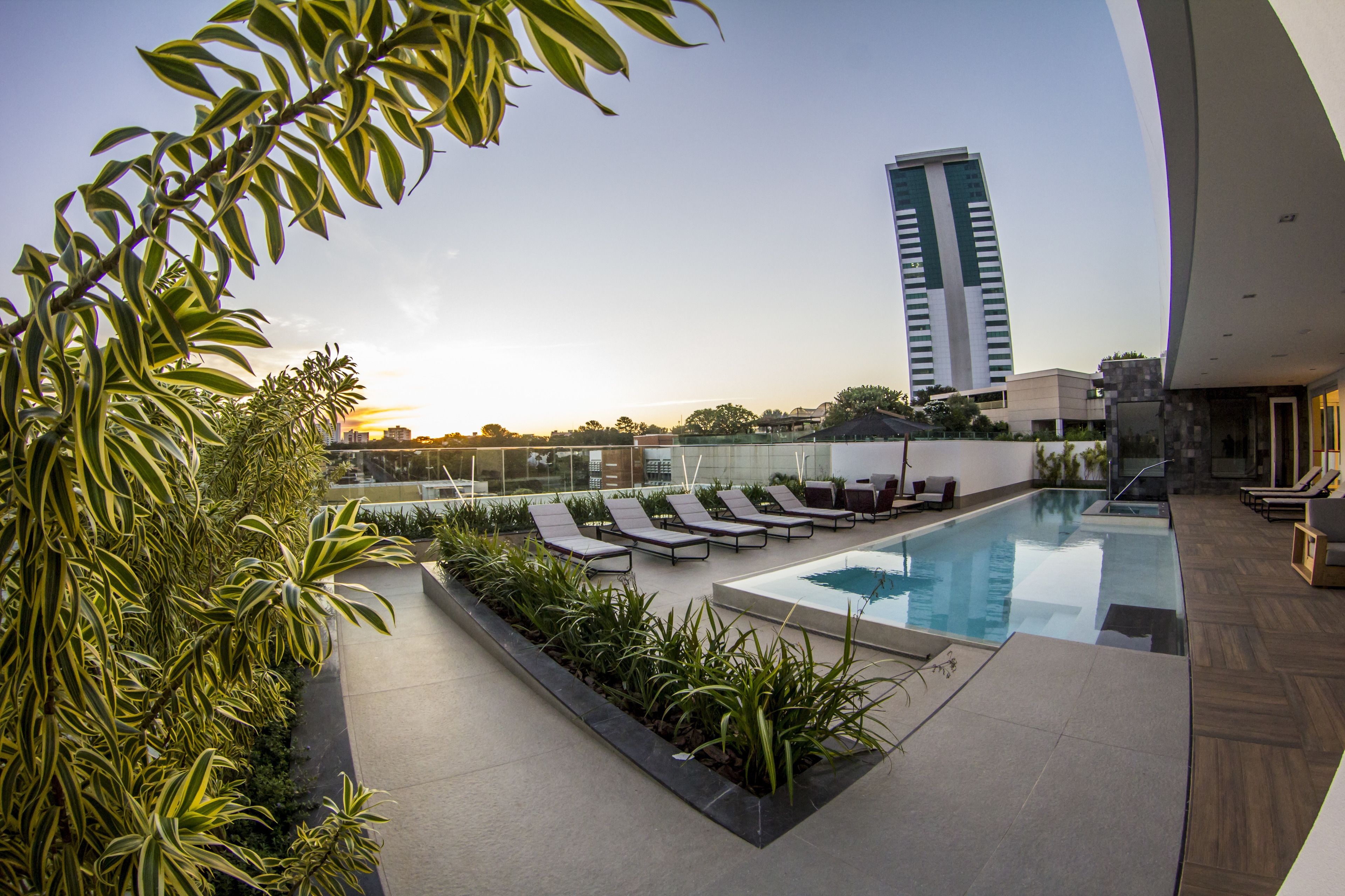 A rooftop pool area with sun loungers, a clear sky, and a modern building in the background.