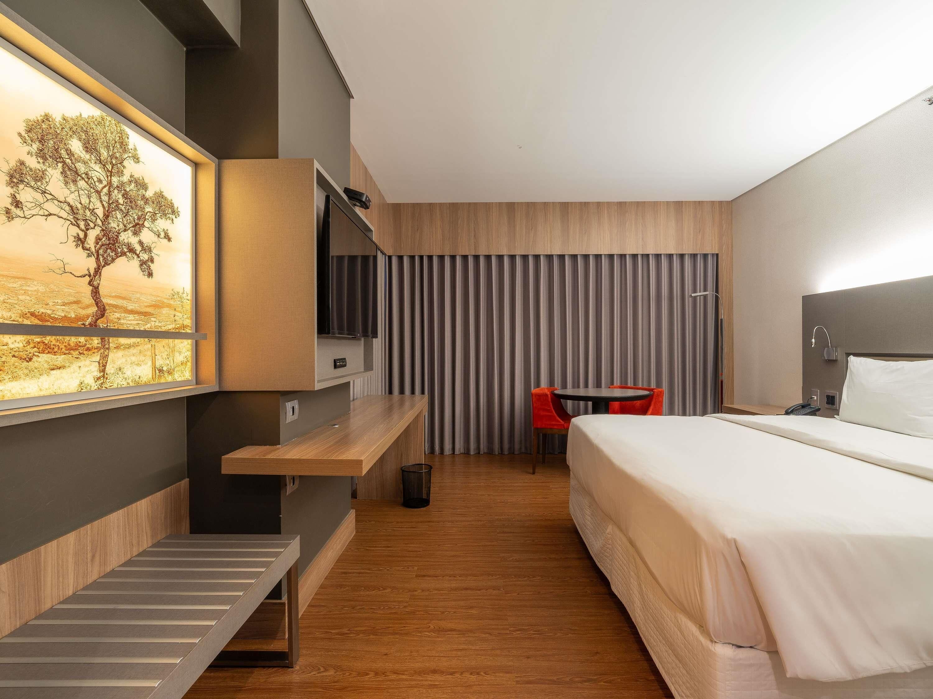 A modern hotel room with a bed, a desk, a chair, a TV, and a window with a desert view.