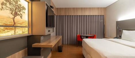 A modern hotel room with a bed, a desk, a chair, a TV, and a window with a desert view.