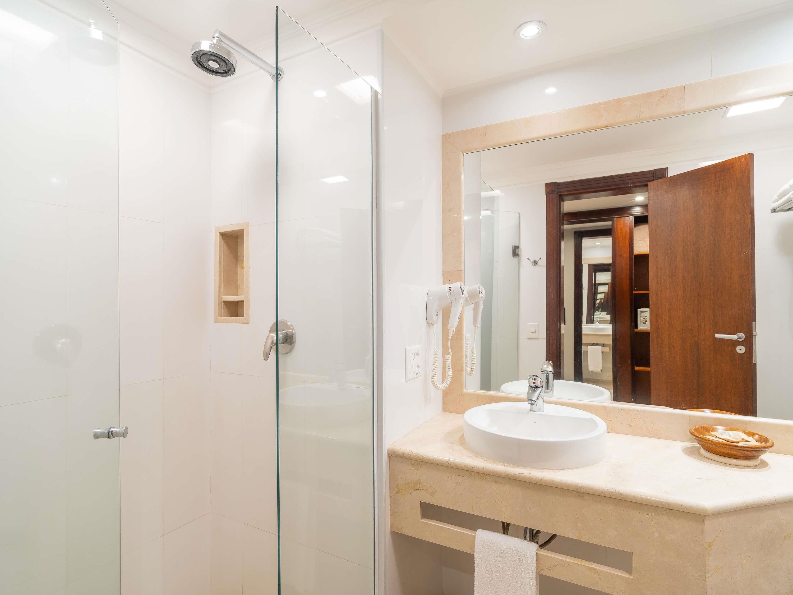 A modern bathroom with a glass shower enclosure, a white sink with a vanity, and a large mirror.
