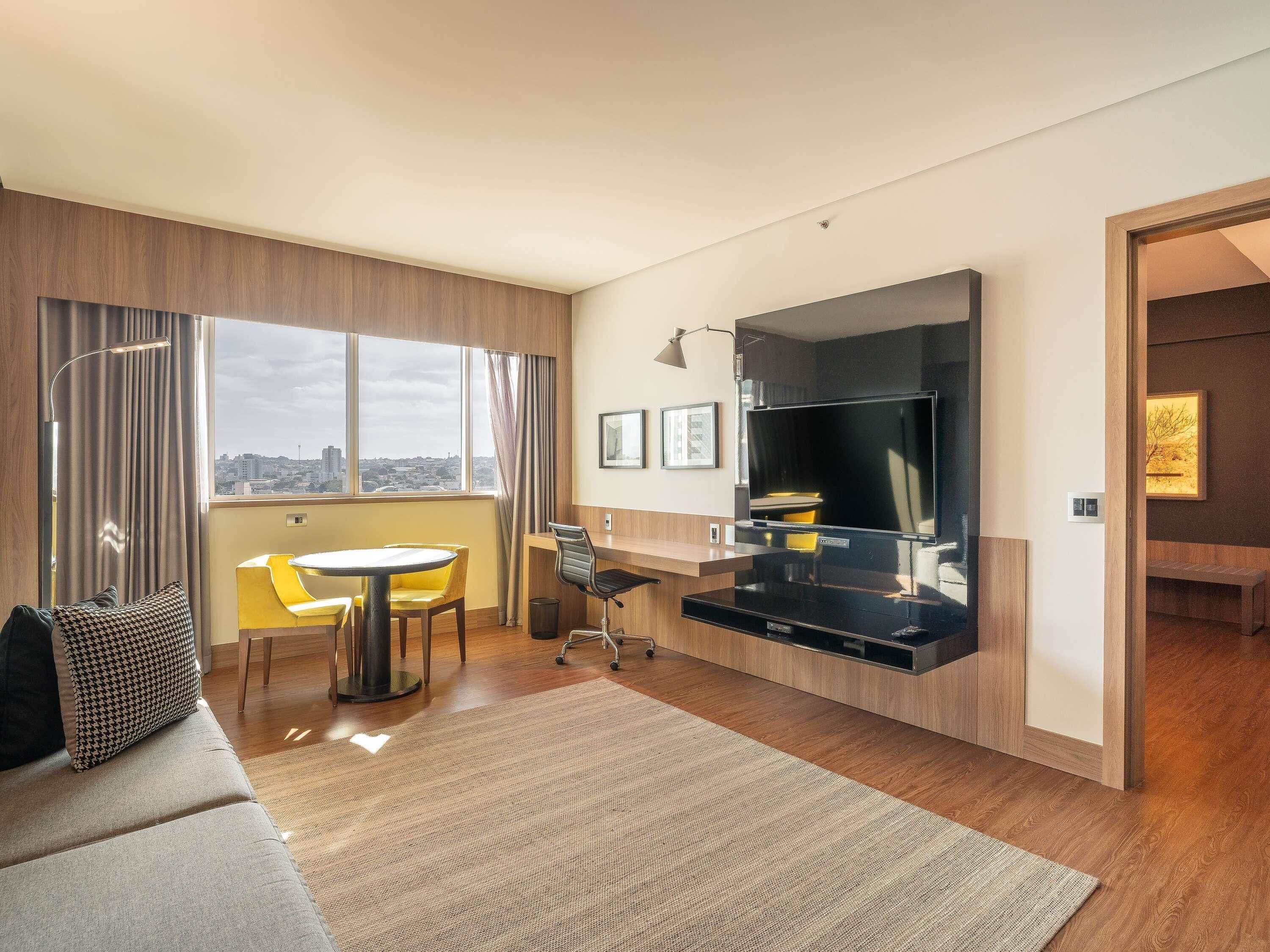 Habitación de hotel moderna con un ventanal grande, un televisor de pantalla plana, una zona de comedor y un sofá.