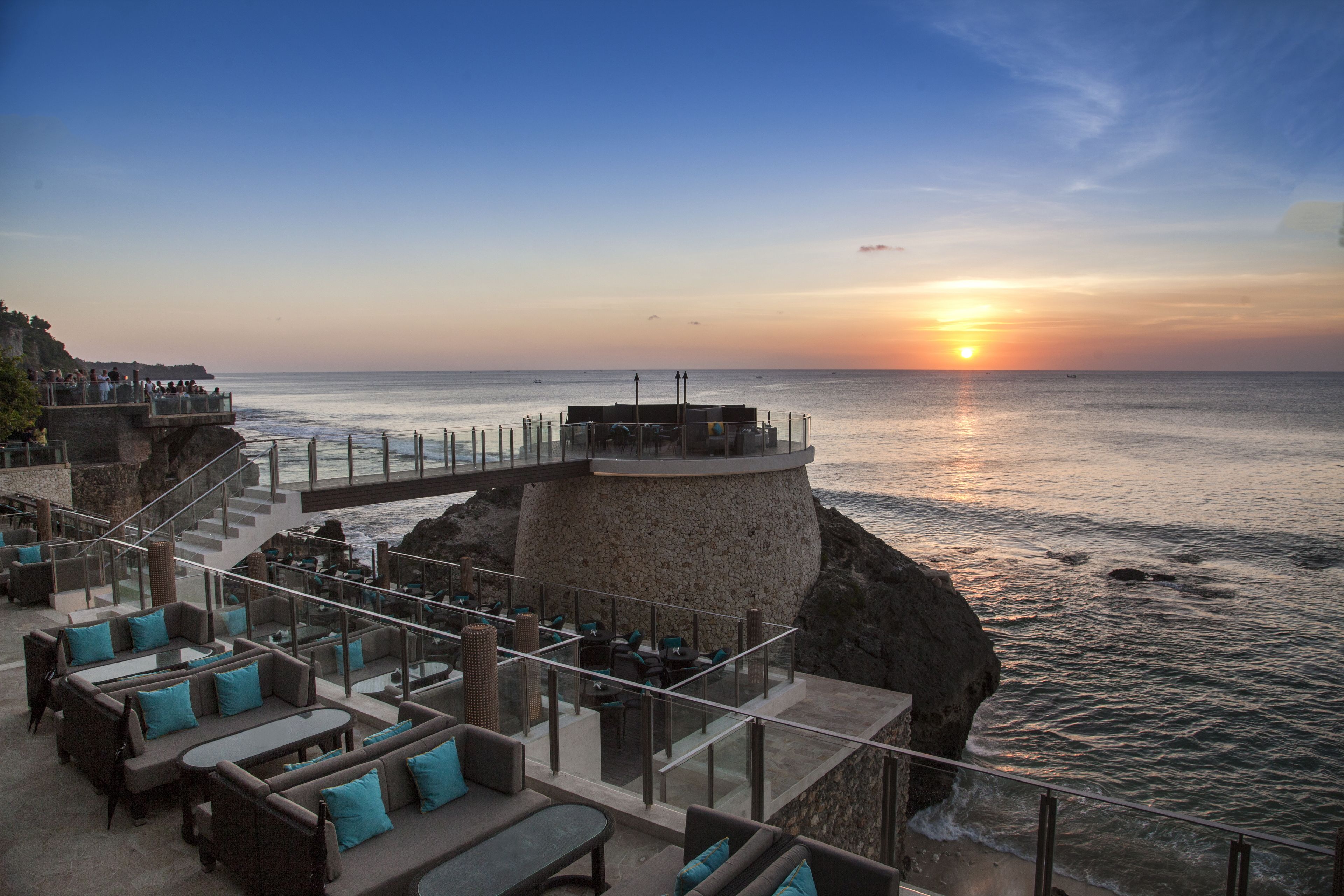 A seaside resort with outdoor seating and a view of the ocean at sunset.