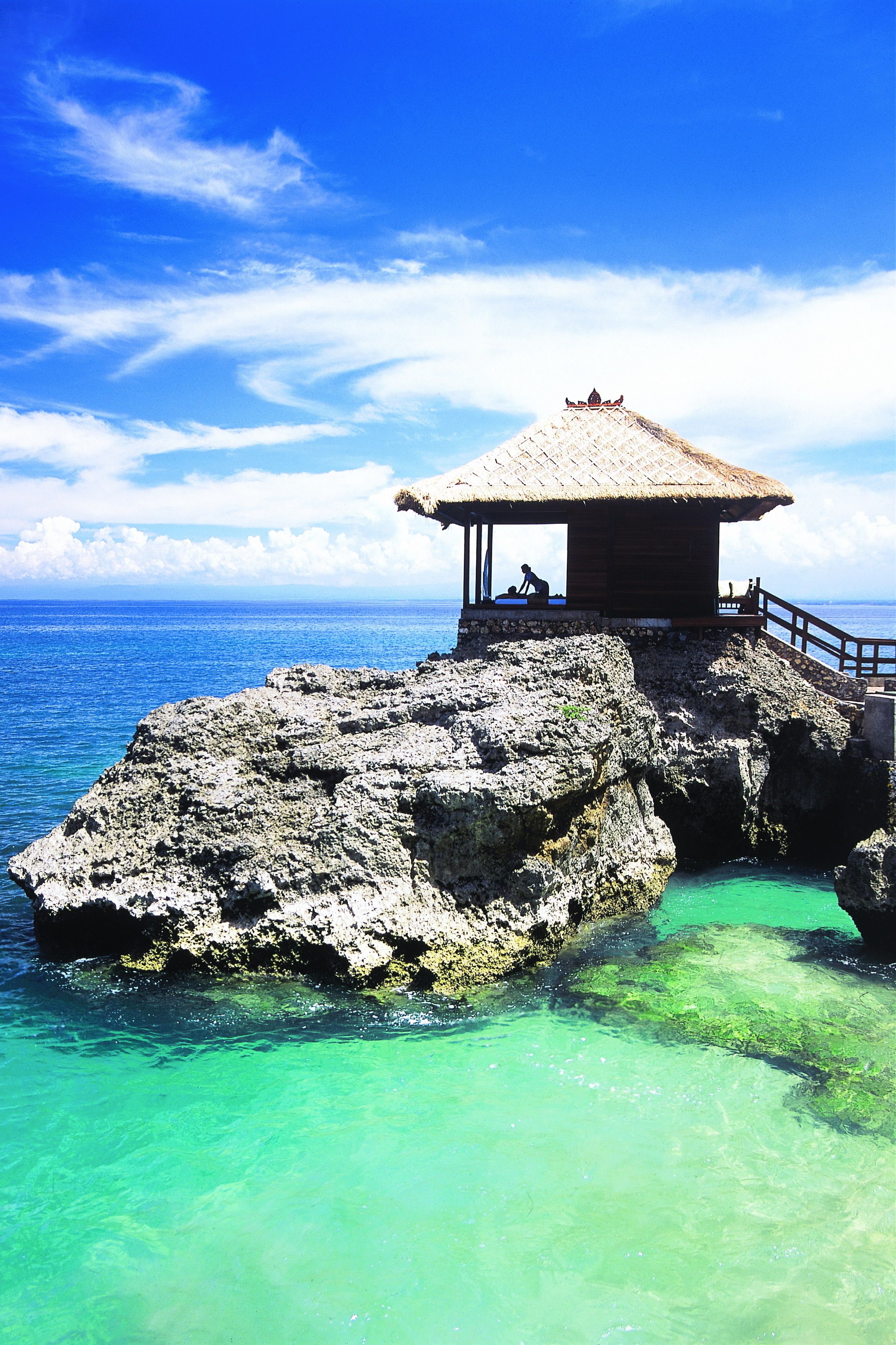 A thatched-roof structure on a rocky outcrop with clear turquoise water.