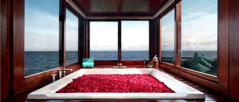 A large bathtub filled with rose petals, wooden walls, and a view of the sea.