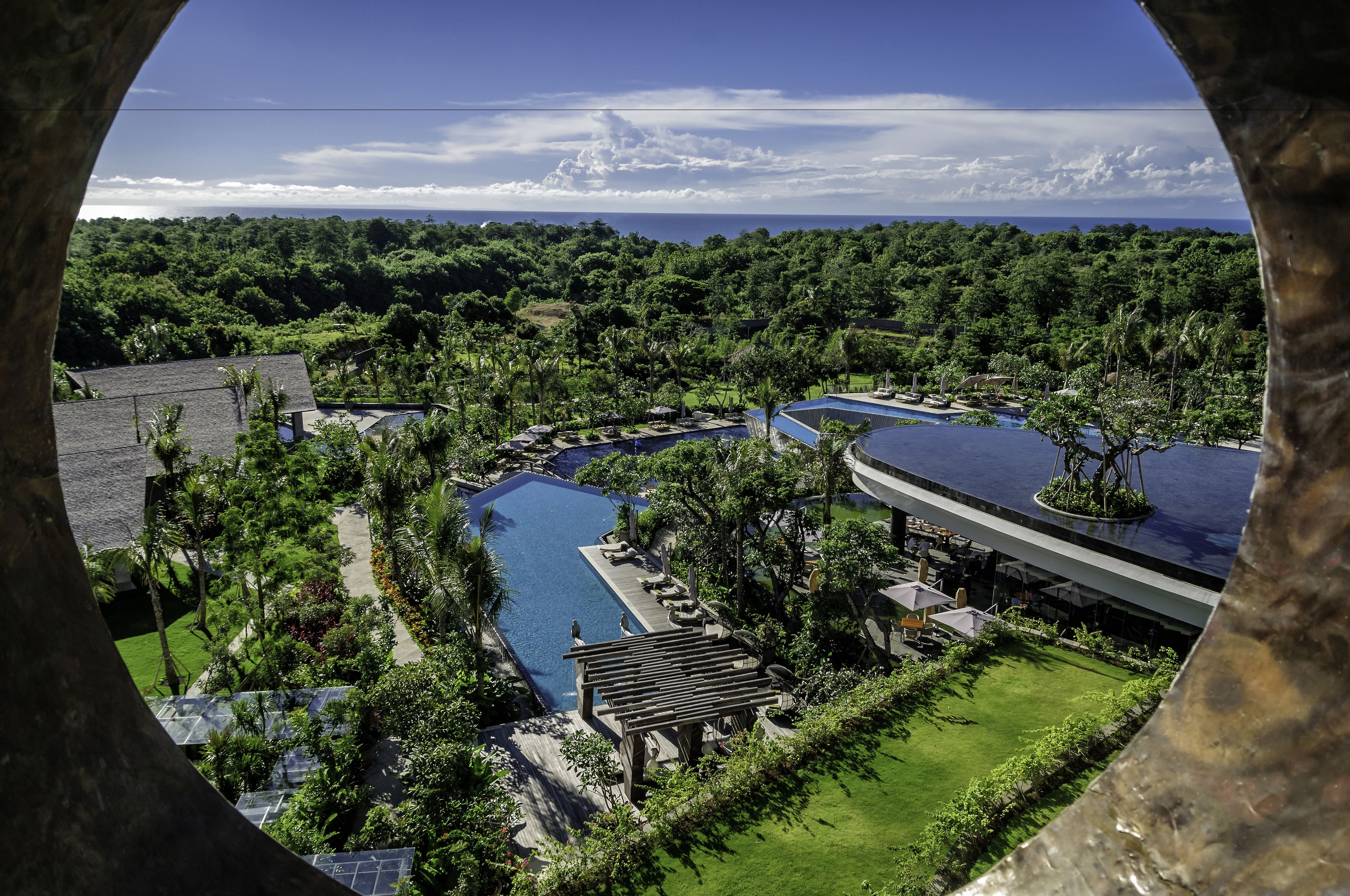 Een resort met meerdere zwembaden, weelderig groen en uitzicht op de oceaan.