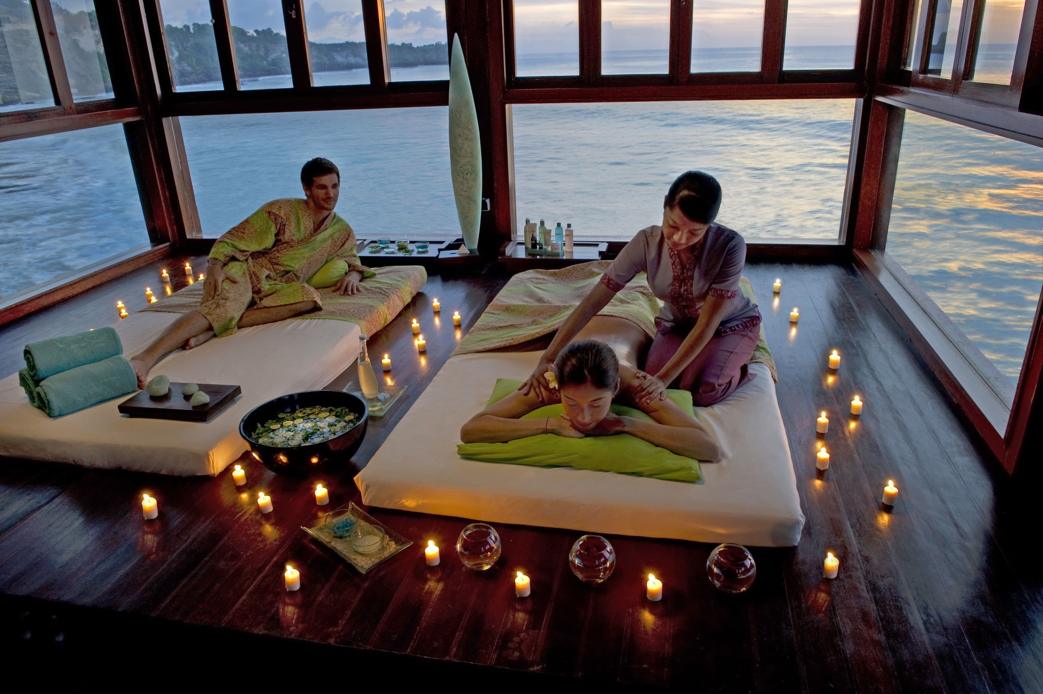A serene spa setting with two individuals receiving massages, a wooden floor, and candles creating a relaxing ambiance.