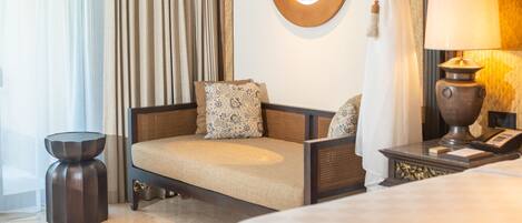 A hotel room with a sofa, a round mirror, a lamp, and a side table.