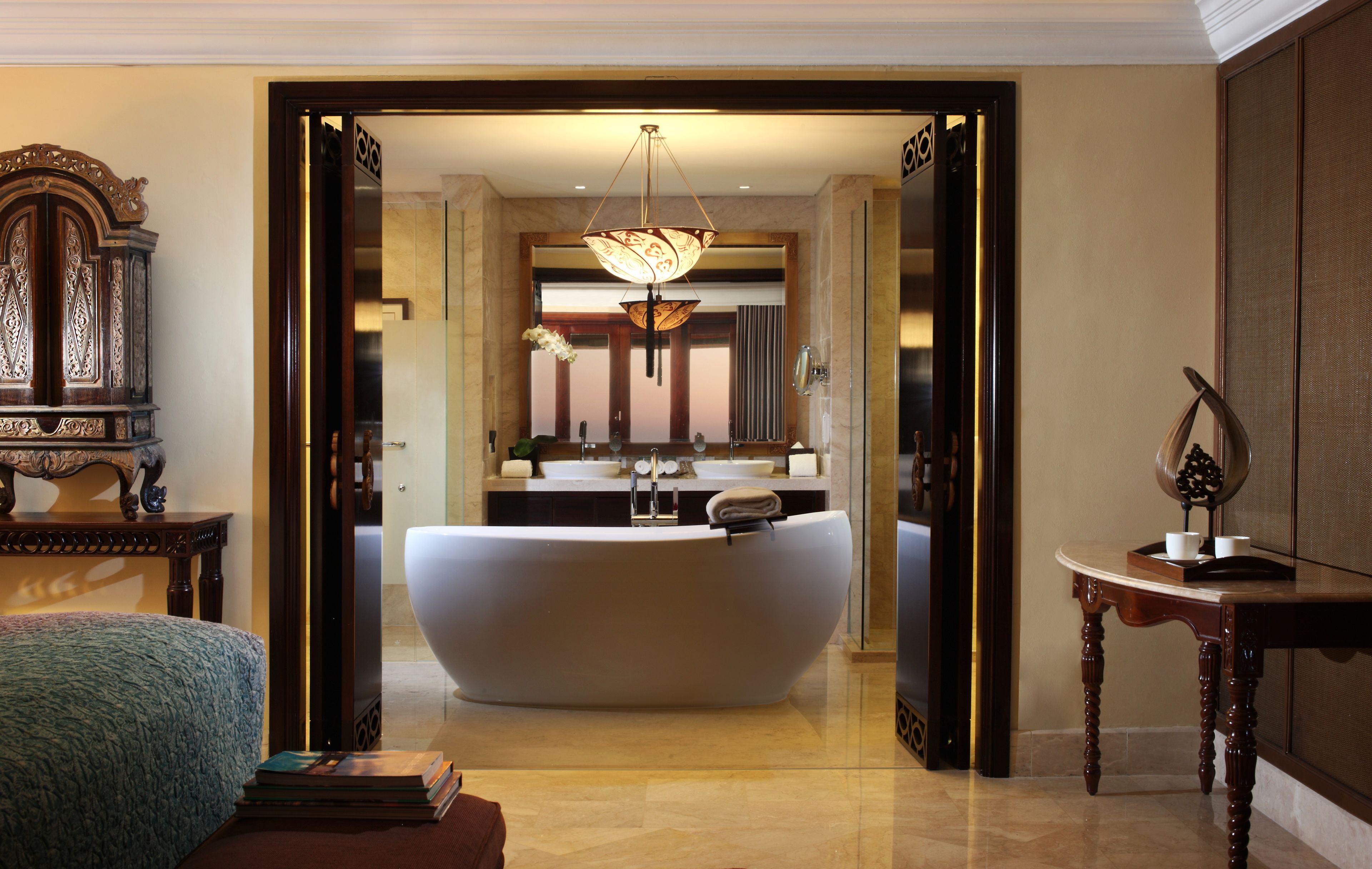 A luxurious bathroom with a freestanding bathtub, a large mirror, and a chandelier.