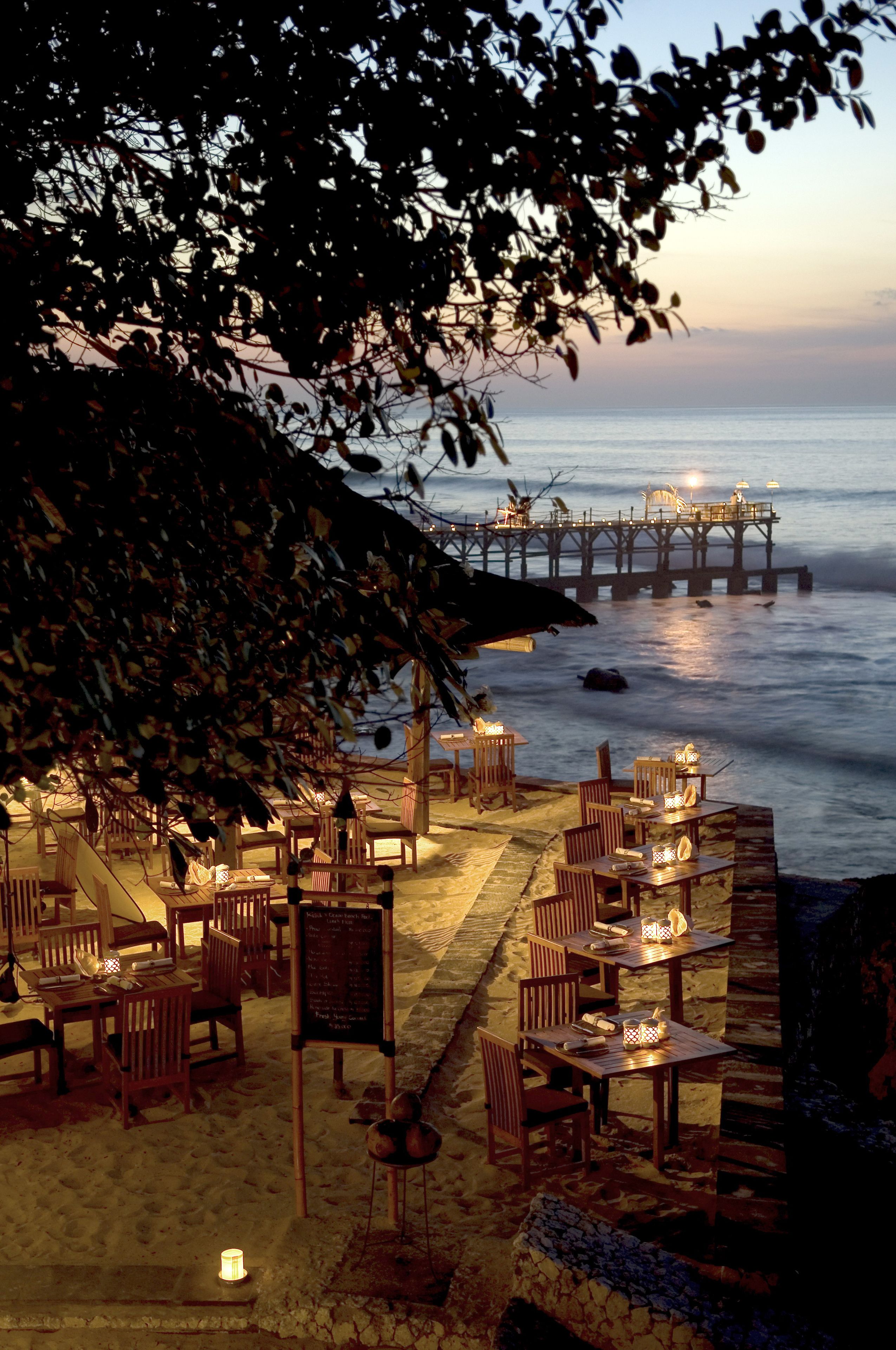 Un espace extérieur aménagé pour les repas, avec des tables et des chaises, offrant une vue sur la mer et une jetée.