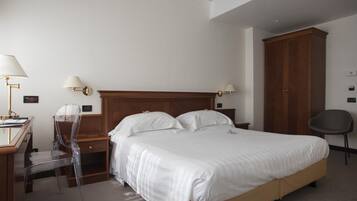 A hotel room with a large bed, a desk with a chair, two wall-mounted lamps, a wardrobe, and a chair.