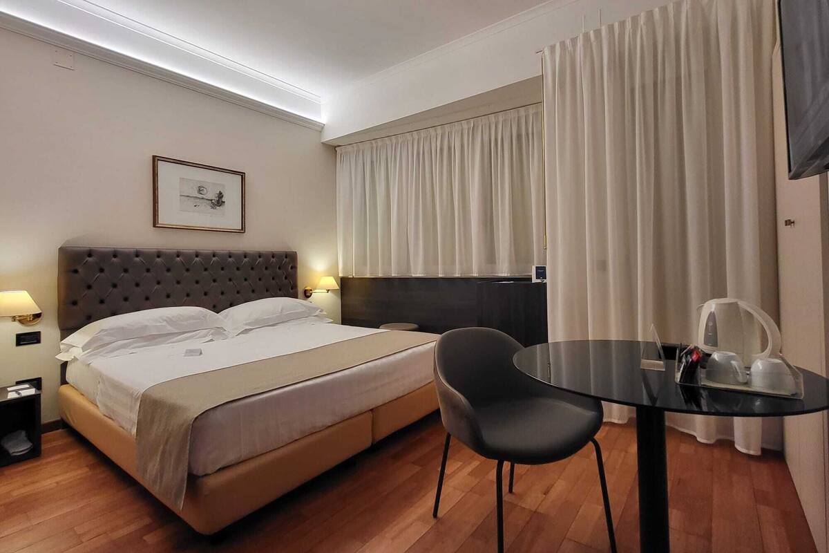 A hotel room with a bed, bedside lamps, a chair, a small table, and a TV.