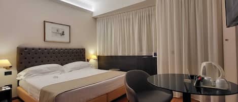 A hotel room with a bed, bedside lamps, a chair, a small table, and a TV.