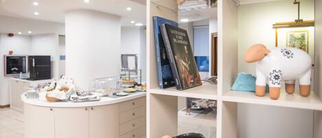 A modern kitchen with a central island, a bookshelf with books and decorative items, and a counter with food and drinks.